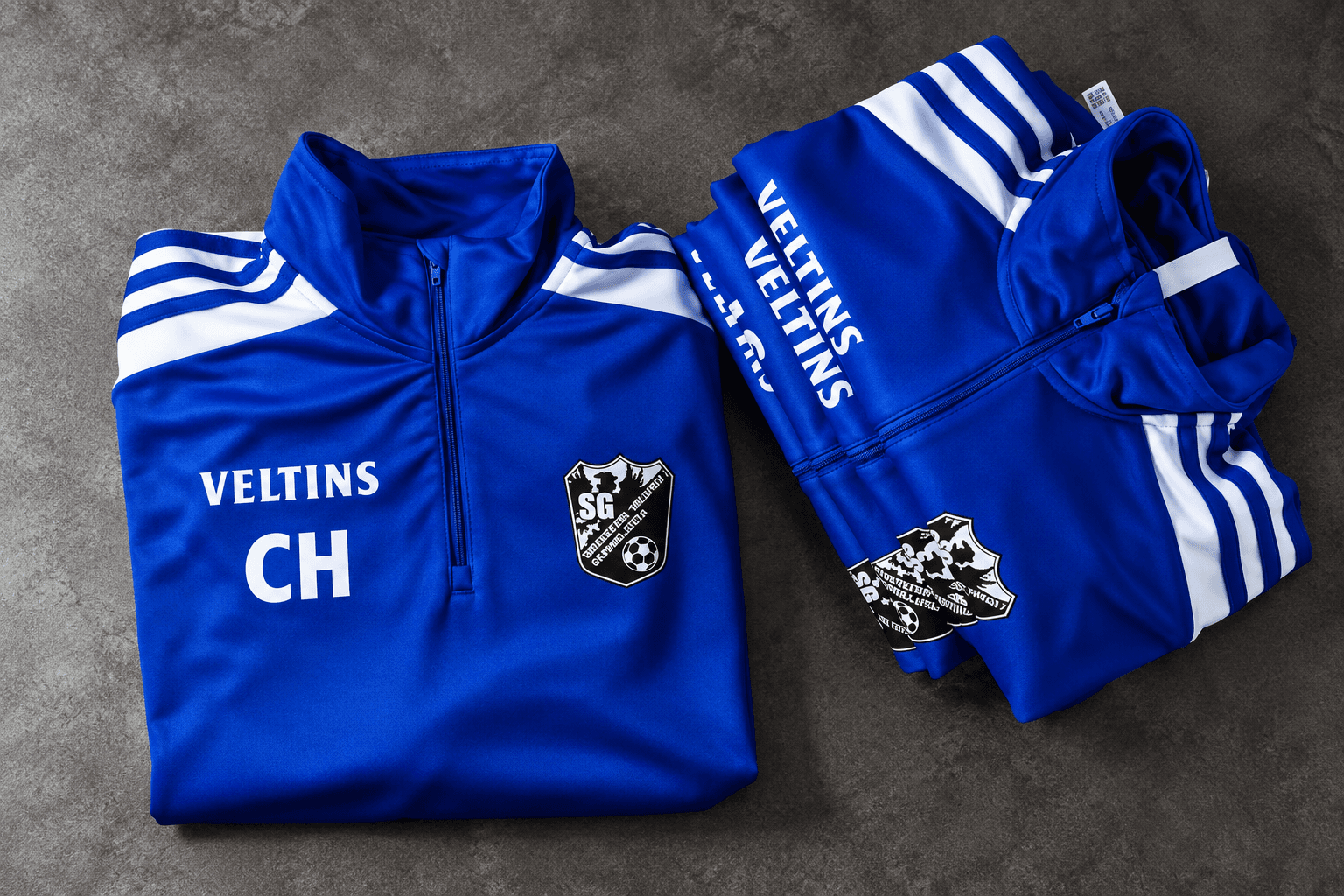 Gestapelte blaue Vereinsoberteile mit Spieler Initialen, Vereinswappen und Sponsorem-Logo